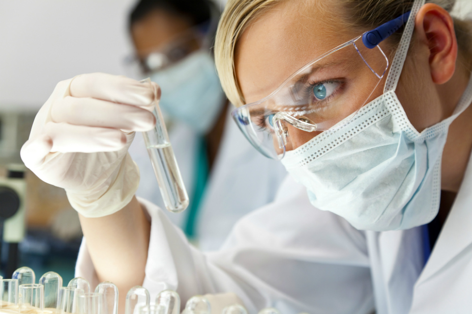 en kvinna med laboratoriekläder och andningsmask studerar ett provrör på nära håll.jpg