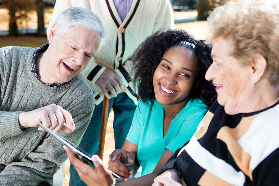 2 Äldre Sitter Med Undersköterska Och Tittar På Skärm Och Skrattar; Lund, Kommun, Digital Hemvård